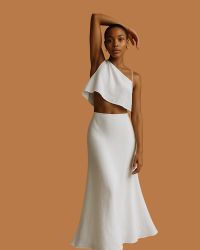 A model wearing an asymmetric one-shoulder crop top and a high-waisted, flowy A-line skirt, both in linen fabric, in a colorless background.